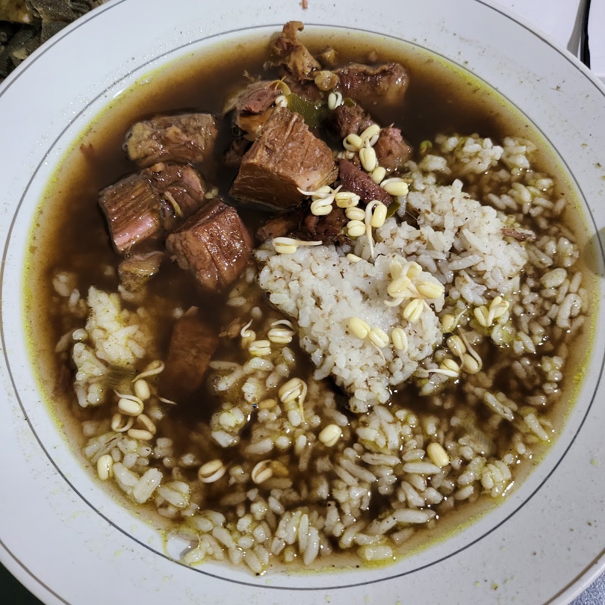 Semangkuk rawon berkuah hitam pekat berisi potongan daging sapi, nasi putih, dan taburan tauge pendek.