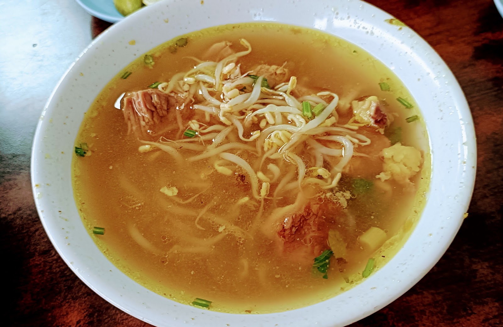 Semangkuk soto daging berkuah kuning bening dengan tauge, irisan daging, dan taburan bawang goreng.