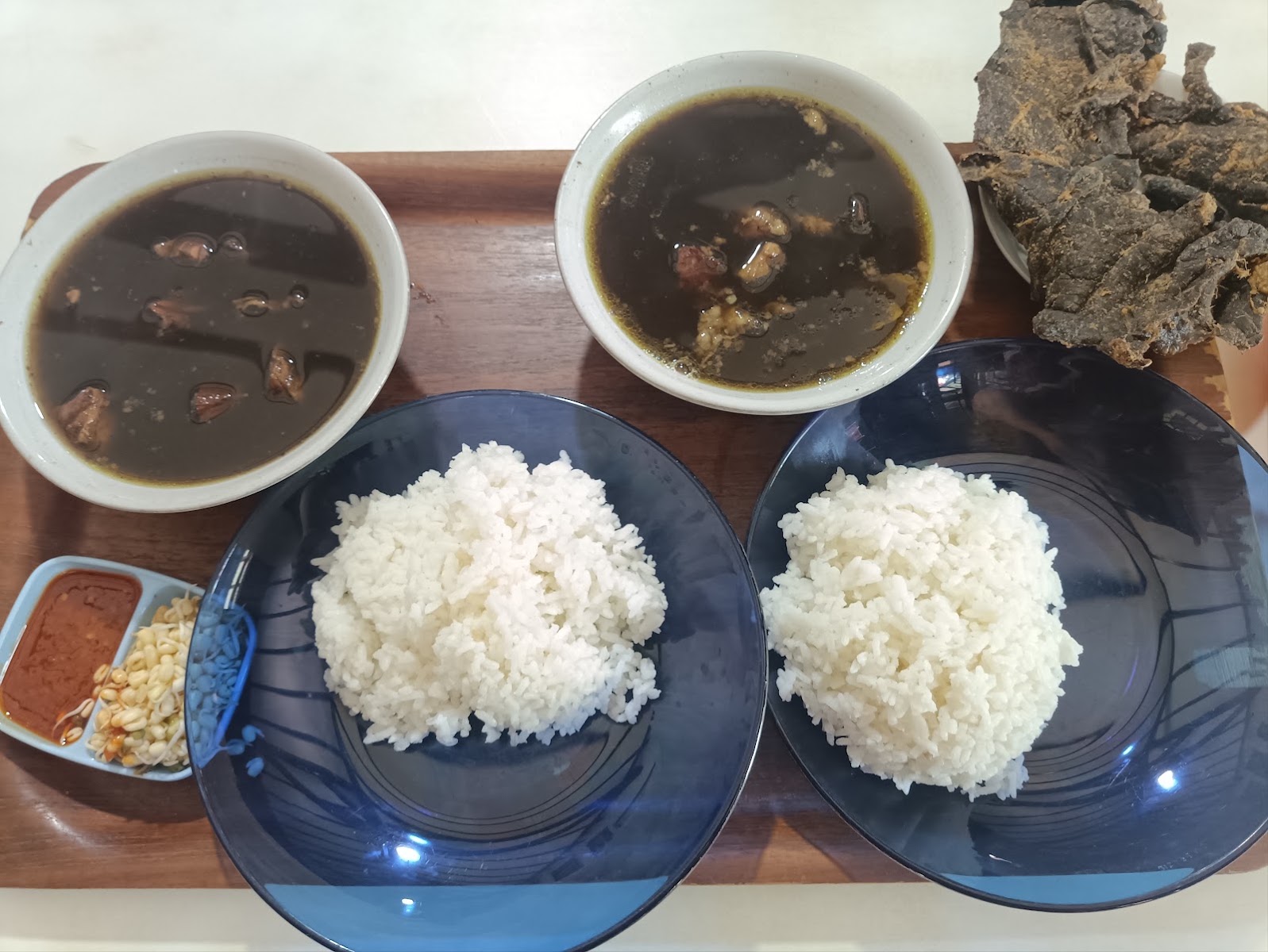 Nampan kayu berisi dua mangkuk rawon, dua piring nasi putih, keripik paru, dan sambal.