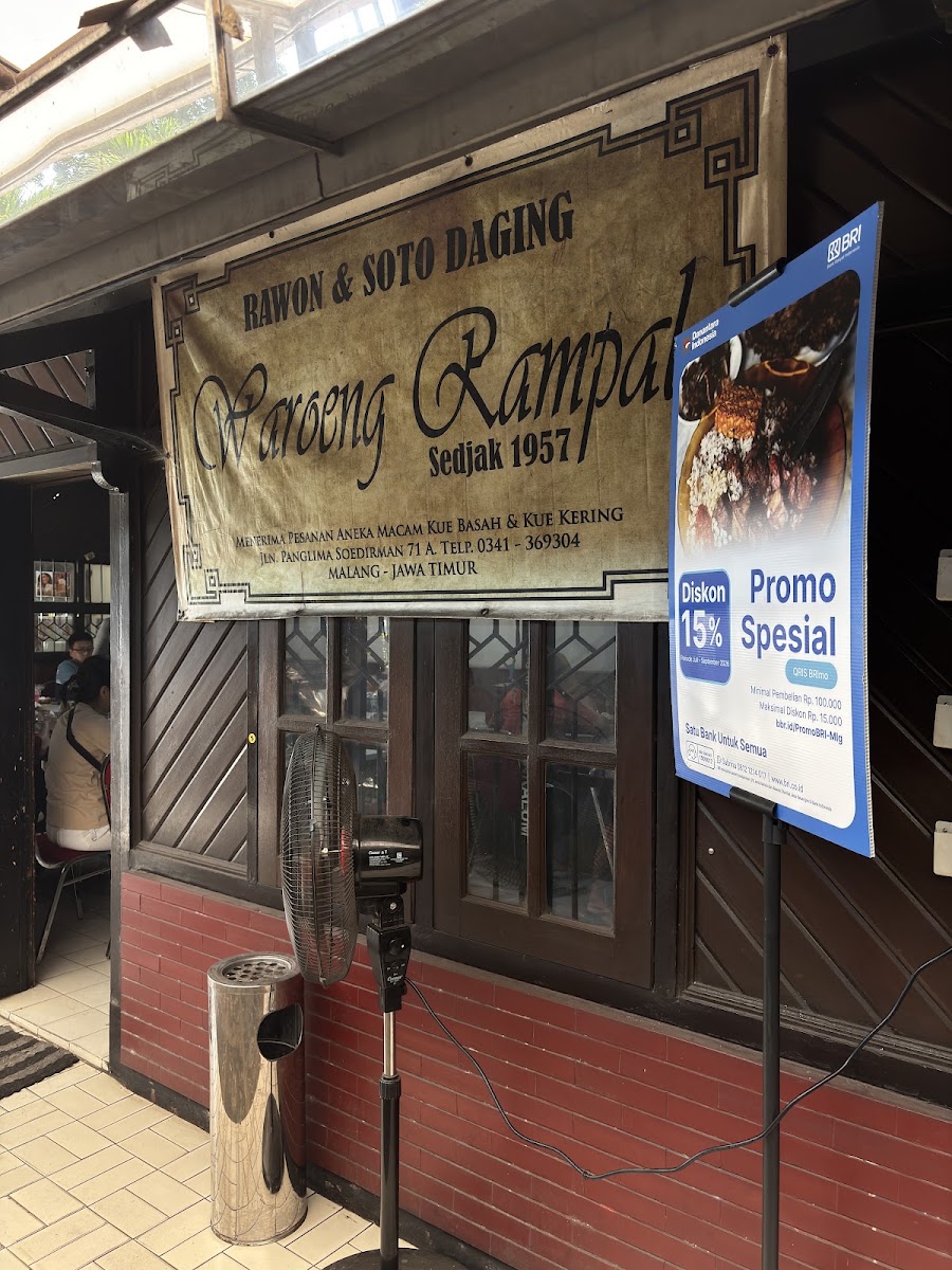 Papan nama Waroeng Rampal bertuliskan Rawon dan Soto Daging serta Sedjak 1957, terpasang di atas etalase depan.
