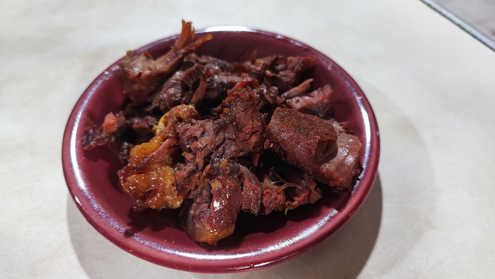 Piring merah tua berisi tumpukan potongan empal dan babat goreng berwarna cokelat gelap.