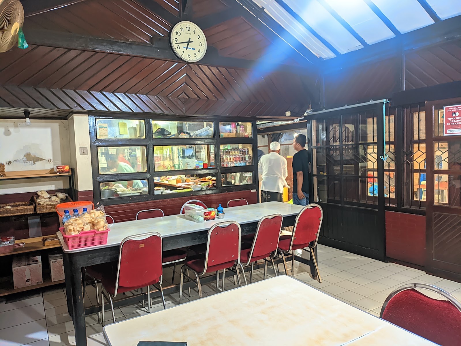 Ruang makan dengan kursi merah, meja panjang berlapis kayu, dan deretan foto berbingkai di dinding.